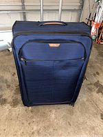 Front view of Ricardo suitcase in blue fabric with brown accents and front zippered pocket.