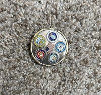 US Military challenge coin with six colored branch emblems and American flag in center against carpet background.