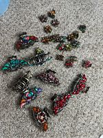 Photo of multiple vintage metal hair claws in various colors and rhinestone decorations spread on carpet.