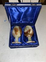 Open blue satin-lined presentation box containing two marble cups with brown and cream natural veining.