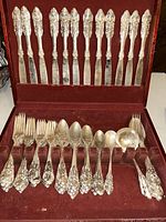 Full set displayed in fitted red velvet case showing top row of knives and bottom row of forks, spoons, serving utensils