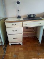 Photo showing white desk with four drawers on left side, glass top surface, small lamp and clock radio on top.