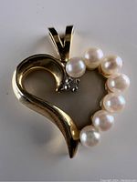 Close-up front view of gold heart pendant with six pearls and one diamond