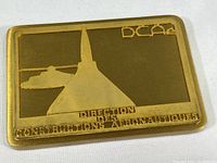Front view of rectangular brass paperweight with embossed design of aircraft and structure along with text.