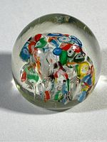 Clear, dome-shaped glass paperweight with colorful embedded fragments in red, blue, green, yellow, and white.