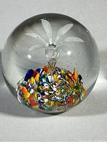 Front view of clear glass paperweight showing colorful millefiori pattern and floral motif inside with one small fleabite near the top.