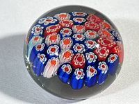 Top view of Murano glass paperweight showing detailed millefiori floral pattern in red, white and blue colors inside clear glass.