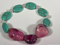 Overview of the full bracelet showing turquoise oval beads, small round white beads, and large polished pink agate stones on elastic cord.