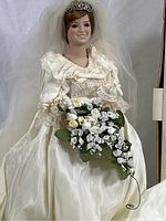 Close-up view of the 18-inch Princess Diana Bride Doll wearing a satin and lace bridal gown, tiara, and veil, holding a bouquet of white and yellow roses.