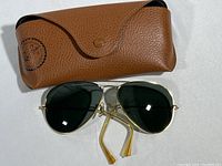 Photo of vintage Ray-Ban Aviator sunglasses with brown leather case. Sunglasses have gold frames, green lenses. Ear grips damaged.