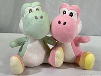 Both Yoshi plush figures in pink and light green colors, showing front and seated positions