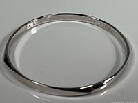 Full view of the smooth silver tone bangle bracelet showing its round shape and signed inside.