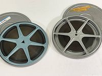 Two 8mm film reels in metal cans with blue spoked plastic reels visible.