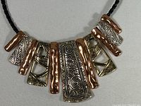 Close-up of the copper and silver tone decorative pendants with detailed patterns on the necklace attached to a black braided cord.