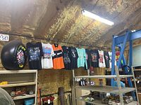 Wide view of multiple large graphic t-shirts hung on a rod inside an insulation-lined garage.