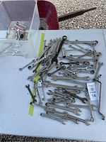 Photo showing a large assortment of different wrenches in varying sizes and types laid out on a white table, including combination wrenches, open-end, flare nut, and specialty wrenches, some are heavily used with metal patina.