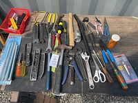 Photo showing assortment of hand tools laid on a black surface including hammers, pliers, screwdrivers, scissors, cutting tools, small hand saw, and pack of diamond files.