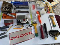 Full view of assorted tools spread on table including sharpening stones, impact driver chuck, universal protractors, vinyl tubing, Dopge license plate, brushes, and measuring tools.