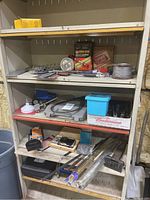 Shelf with multiple tools, boxes, and hardware including clamps, fork set, and metal tools scattered on shelves