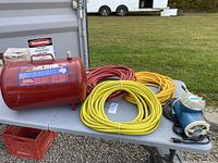 Wide view of the portable air tank alongside three air hoses and electric compressor pump on table outdoors.