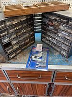 Photo showing the two black plastic hardware organizer containers with multiple small drawers filled with assorted metal hardware, also showing the new flaring toolkit in blue packaging and the wooden divided container on top.