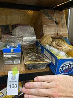 Photo of various household items on shelf including a box of rope and twine, a decorative metal grille piece, and wrapped spray gun box.