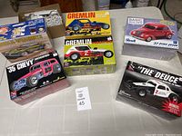Six model car kits, boxes shown with colorful illustrations, one box opened showing unassembled plastic parts.