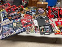 Overview of NASCAR memorabilia laid out on table including die-cast cars, collector plates, books, and banners.