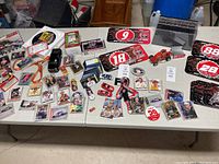 Table with NASCAR memorabilia including playing card tins, collectible cards, small model cars, stickers, and more items.