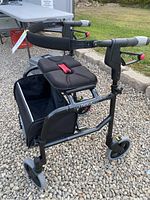 Front-left perspective showing padded seat with red Nexus strap, storage bag, and wheel configuration.