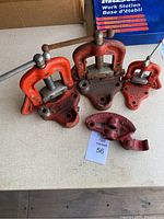 Photo showing three red pipe clamps with wooden handles and one red bender head on a table.
