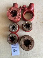 Top down view of the six pipe threading dies, showing two large red cast iron die holders and four smaller round threading dies with adjustable screws. Surface rust and wear visible.