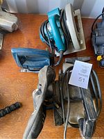 Makita circular saw, sabre saw and belt sander together on a wooden surface.