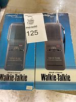 Two Realistic TRC-91 walkie talkies on top of their original blue boxes, showing front view and product labeling.