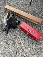 Photo showing two unopened boxes of metal sawhorses, a red toolbox, and an electric saw on gravel surface.