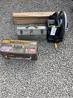 Top view of lots with circular saw, two metal toolboxes, and boxed new sawhorses on gravel