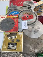 Photo showing multiple saw blades stacked and overlapping with visible branding including Jobmate, Craftsman and Skil, mostly 7 1/4 inch size