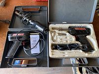 Three vintage electric soldering guns in cases with cords visible, showing included items and overall condition.