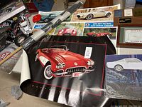 Overview of three car posters and metal signs including a red 1959 Corvette poster and a Ford woodie sign.