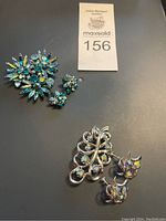 Two brooches and two pairs of matching earrings on black background with MaxSold lot tag