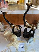 Overview of four animal figurines on table: two black and gold giraffes, ivory bull, small gray animal