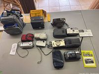 Full lot image showing 8 assorted vintage cameras on table, some with cases and boxes.