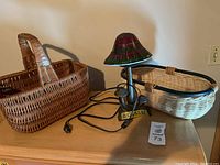Photo showing the mushroom-shaped lamp with stained glass shade alongside two wicker baskets, one white oval and one brown rectangular.