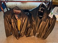 Two black Danier leather jackets hanging on hangers, showing overall fronts and collars.