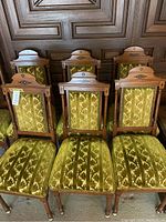 Front view of six dining chairs with gold patterned upholstery and wooden frames.