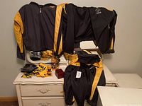 Photo showing two Hamilton Tiger-Cats black and yellow jackets and matching pants on a white dresser, along with bandanas, bobbleheads, and a watch.