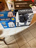 Black & Decker cordless kettle and Farberware utensil set in original boxes on a table.