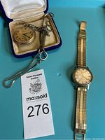 Overview of Longines wristwatch, Hamilton pocket watch in case, chain and utensil on blue background