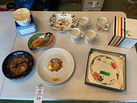 Overview of all items on table: 4 floral mugs, 6 assorted plates and bowls with various floral, bird, and fruit designs, one boxed plate.