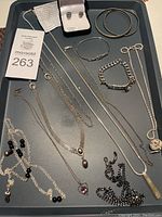 Full overview of the jewelry lot showing multiple silver chains, bracelets, earrings, and eyeglass holders on a black tray.